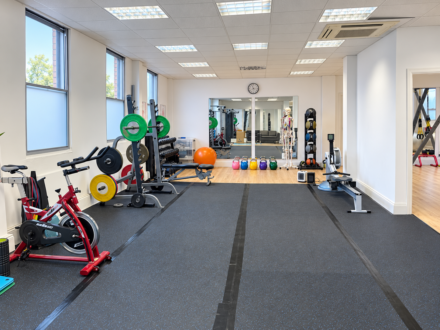 Training floor in the Reigate studio with barbell rack, weight plates, kettlebells, bike and rowing machine